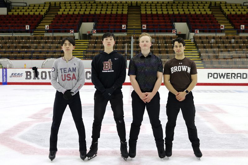 Four members of the Brown Figure Skating Club standing on the ice at Meehan Auditorium, empty stands behind them; Emmanuel Colmenares on the right in a brown Brown T-shirt.