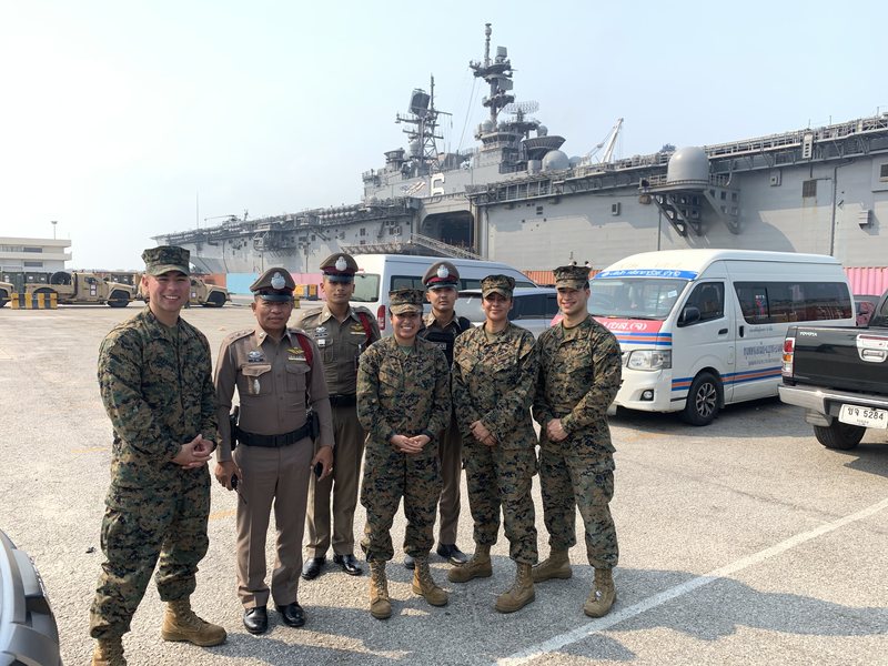 Emmanuel Colmenares with four other Marines and three Royal Thai Police officers on a pier, the amphibious assault ship USS America docked behind them.