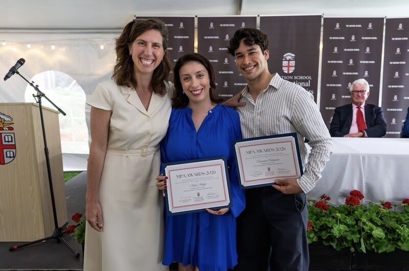 Emmanuel Colmenares and Nicole Nehiley holding MPA Awards 2026 certificates under a tent at the Watson School, with Professor Nicole Pangborn beside them.